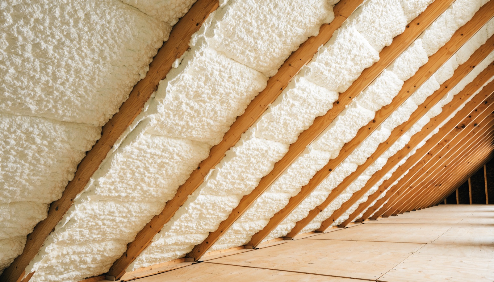 The underside of a roof deck in an attic covered with pale expanded spray foam insulation between the rafters
